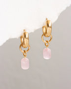 Gold hoop earrings with pink stone drops on a light gray background