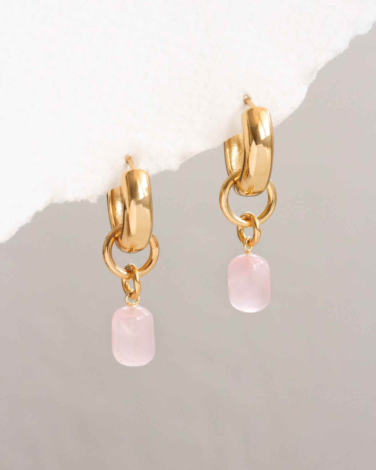 Gold hoop earrings with pink stone drops on a light gray background