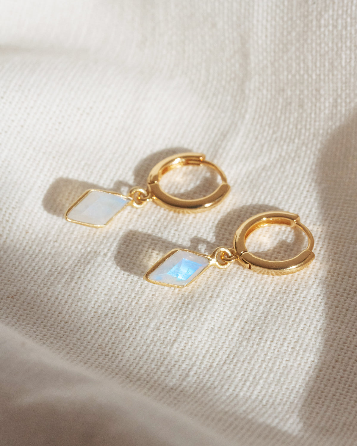 Gold hoop earrings with moonstone stones on a beige fabric background