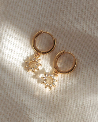 Gold hoop earrings with sun-shaped charms on a beige fabric background