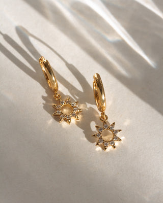 Gold hoop earrings with sun-shaped charms on a light background