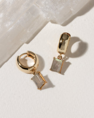 Gold hoop earrings with square gemstones on a light background