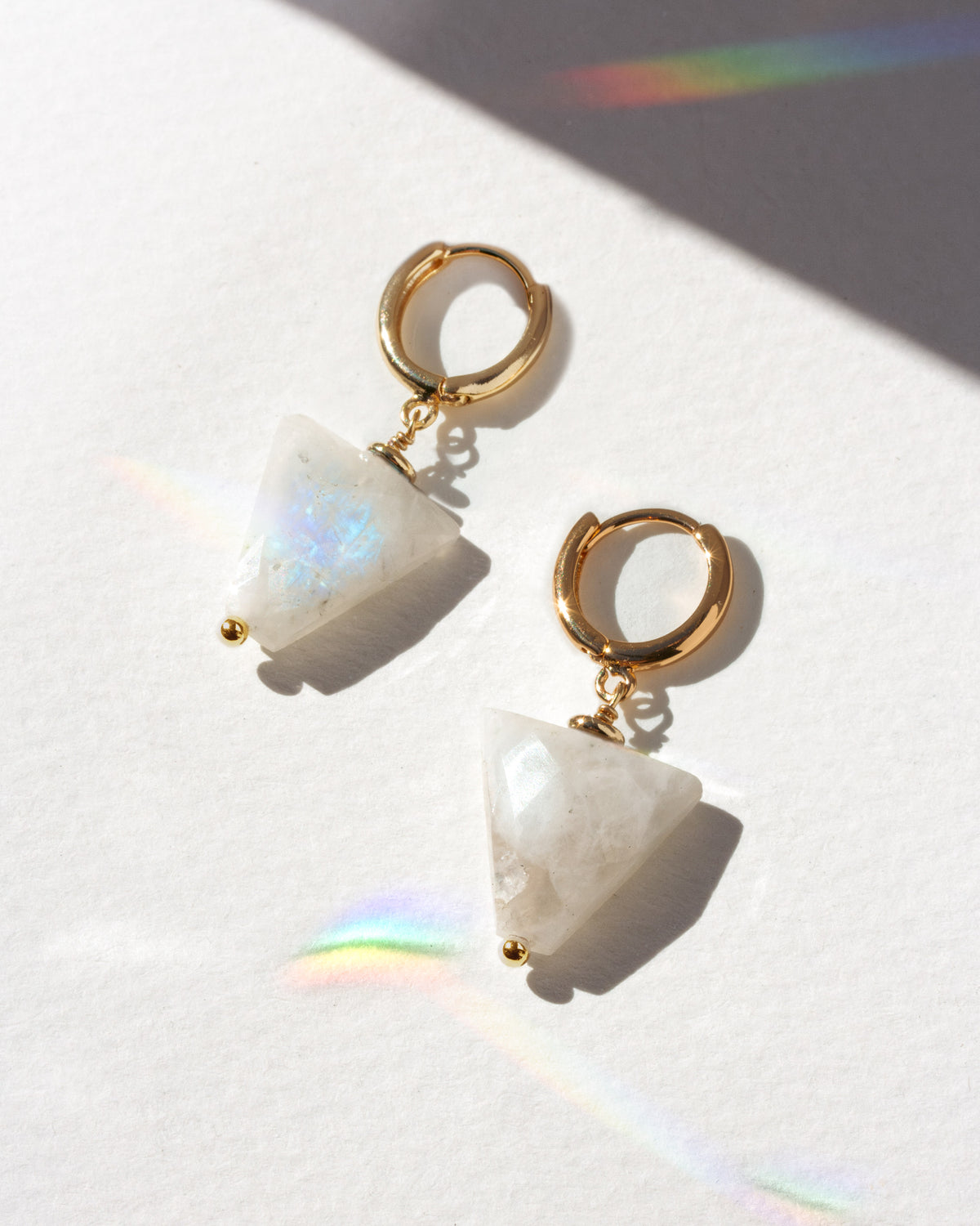 Pair of earrings with gold hoops and moonstone gemstones on a white background
