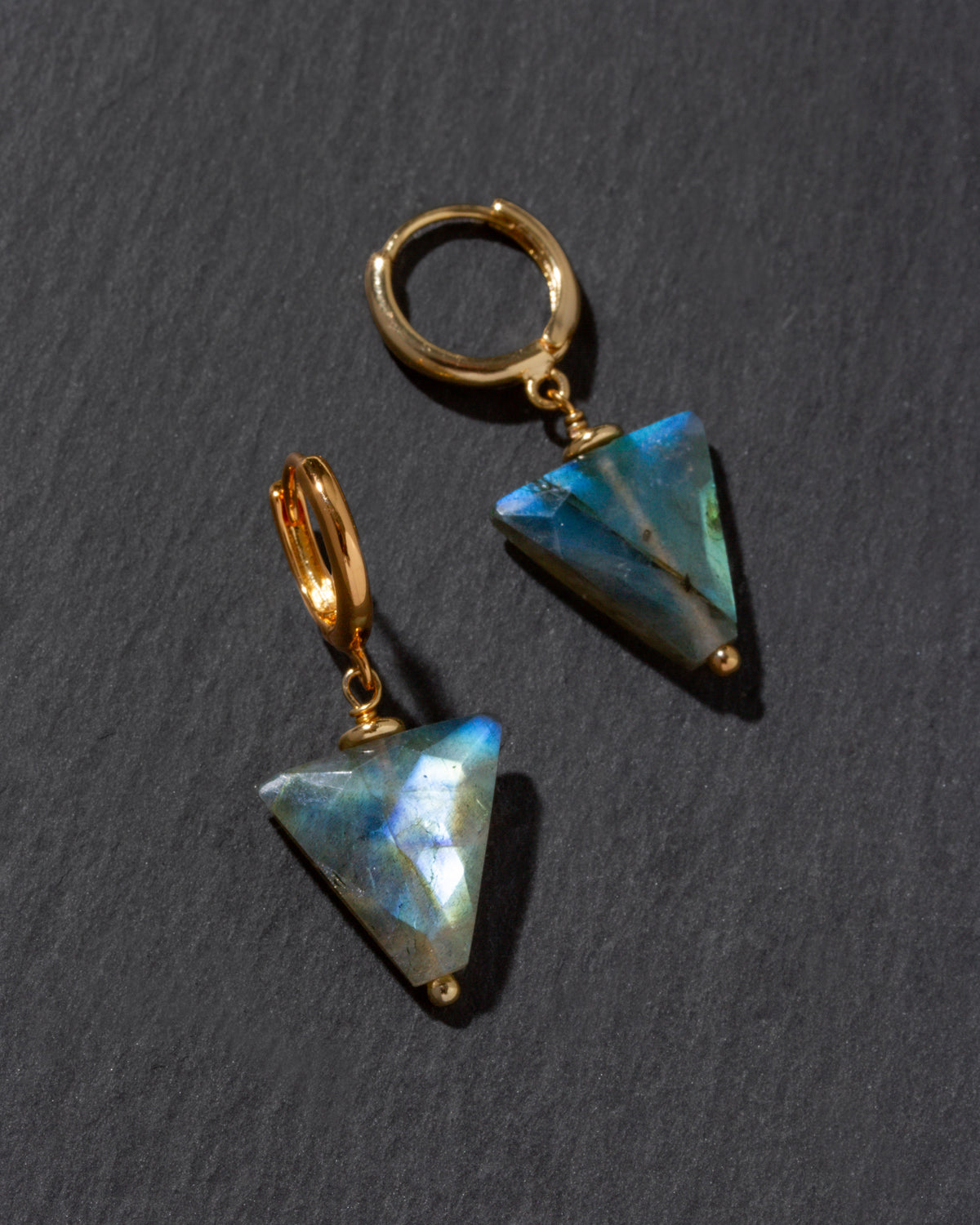 Gold earrings with triangular labradorite gemstones on a dark gray background