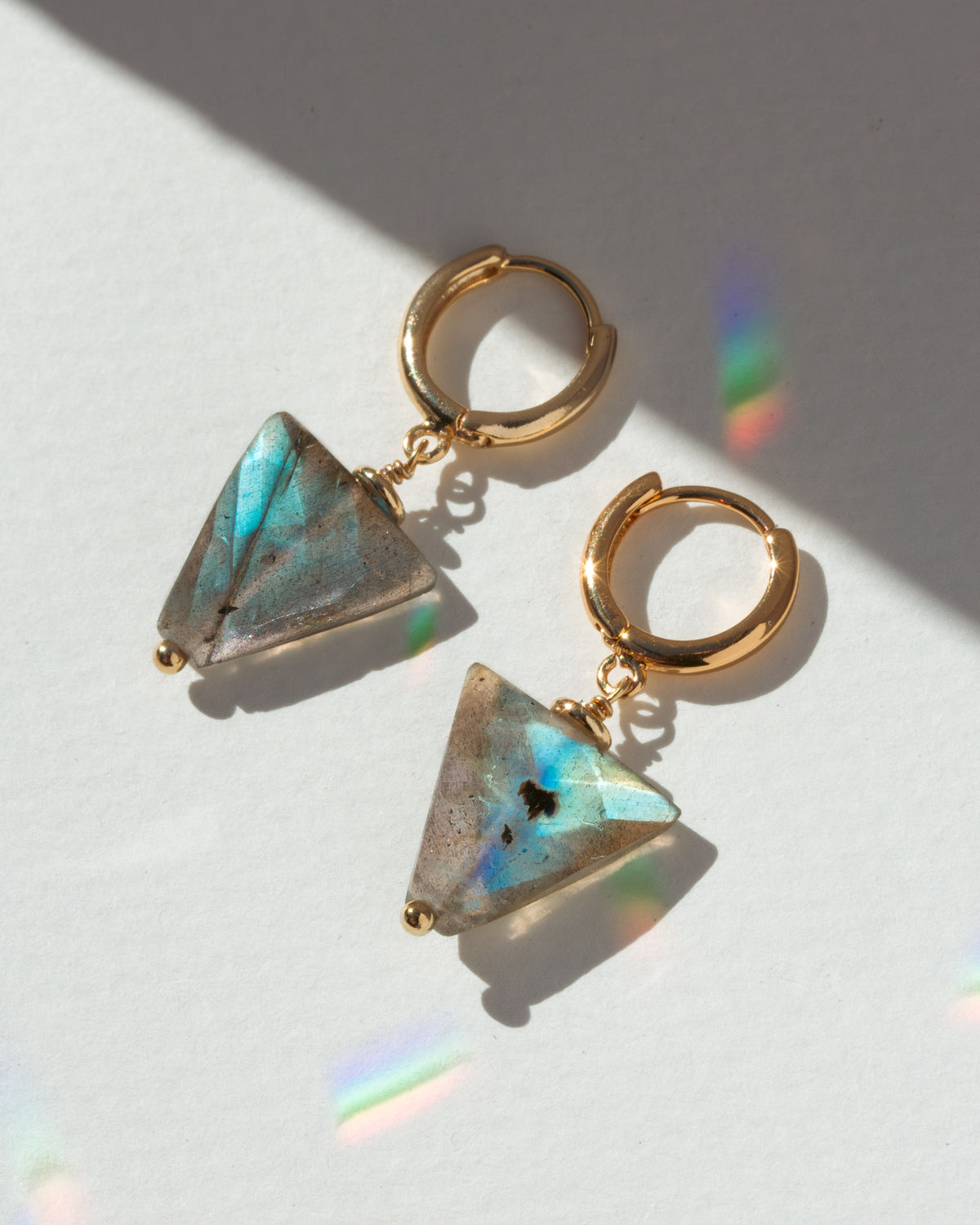 Gold hoop earrings with triangular gemstones on a light background