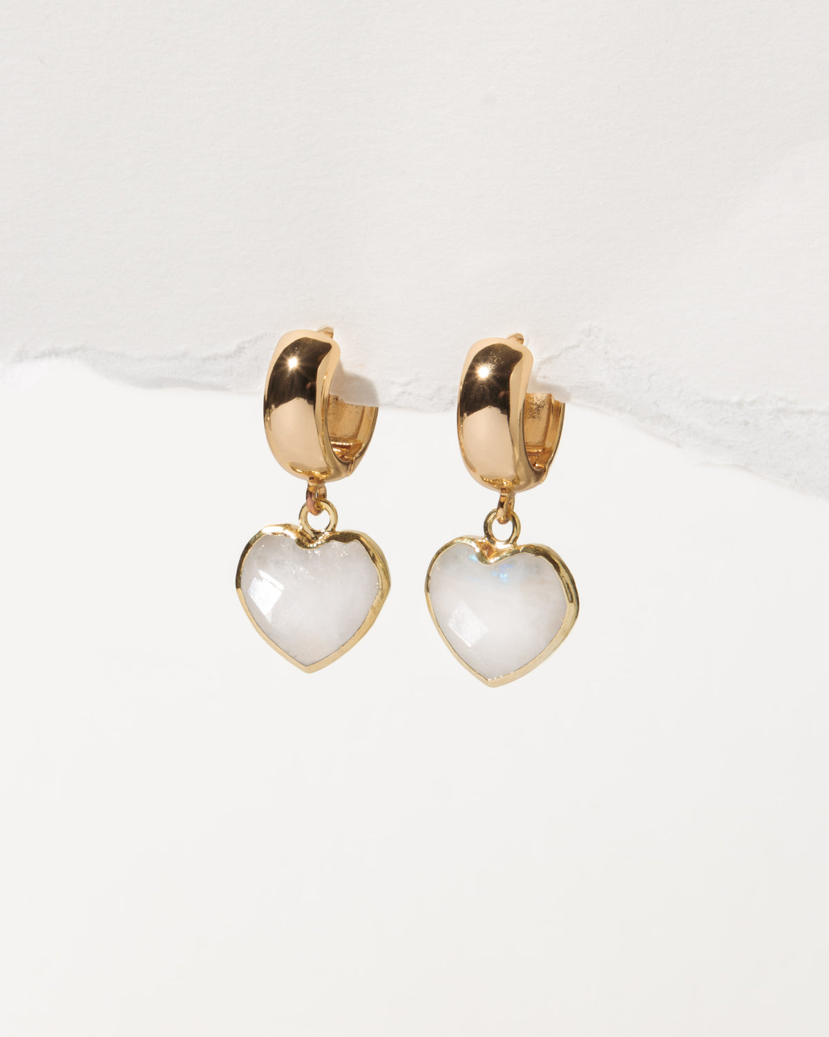 Heart-shaped earrings with gold wide huggie hoops on a white background
