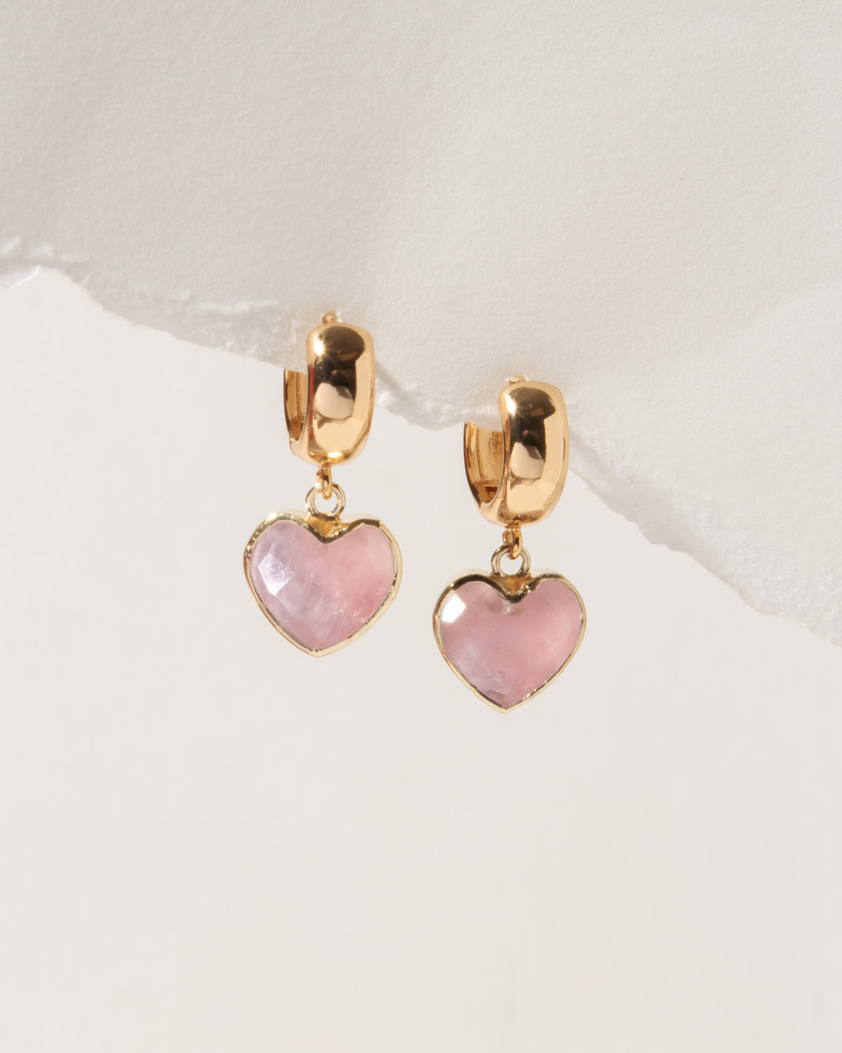 Heart-shaped earrings with pink stones and gold accents on a light background