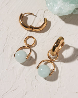 Gold hoop earrings with light blue gemstones on a textured white surface.
