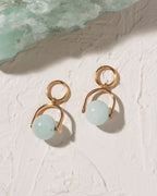 Gold earrings with light blue spherical beads on a textured white surface.