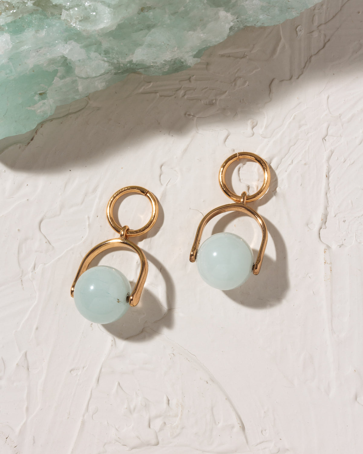 Gold earrings with light blue spherical beads on a textured white surface.