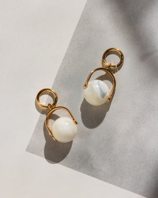Gold earring charms with white mother-of-pearl shell beads suspended from gold arc charm rings