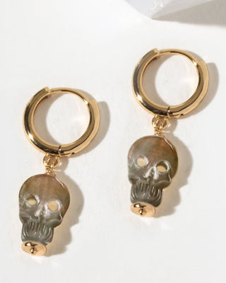 A pair of gold hoop earrings with dangling black lip mother of pearl skull charms.