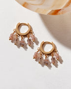 Gold huggie hoop earrings with dangly coffee moonstone beads on a white surface.