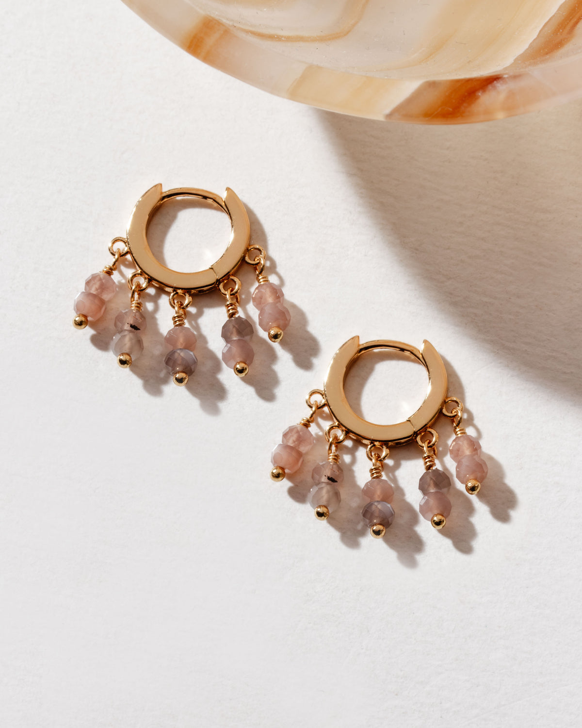 Gold huggie hoop earrings with dangly coffee moonstone beads on a white surface.