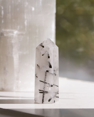 Tourmalinated min quartz obelisk tower on a white surface with blurred background.