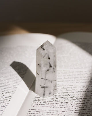 A mini tourmalinated quartz tower with dark inclusions, placed on an open book under natural lighting.