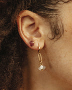 Ear with gold-plated mismatched earrings, one a red stud, the other a white quartz on a gold link.