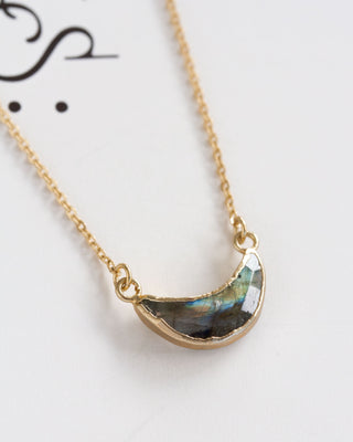 Gold necklace with a semi-circular crescent labradorite moon pendant on a white background