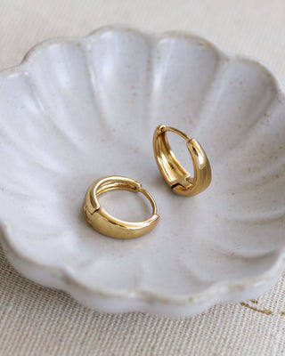 A pair of gold-colored hoop earrings placed on a white, scallop-edged plate.