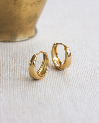 Pair of gold hoop earrings siting on a textured surface.