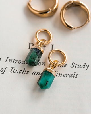 Interchangeable hoop earring charms with green emerald pendants attached to gold-colored hoops, displayed on a paper with text.