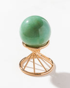 Green aventurine sphere curio sitting on a gold colored stand on a white surface.