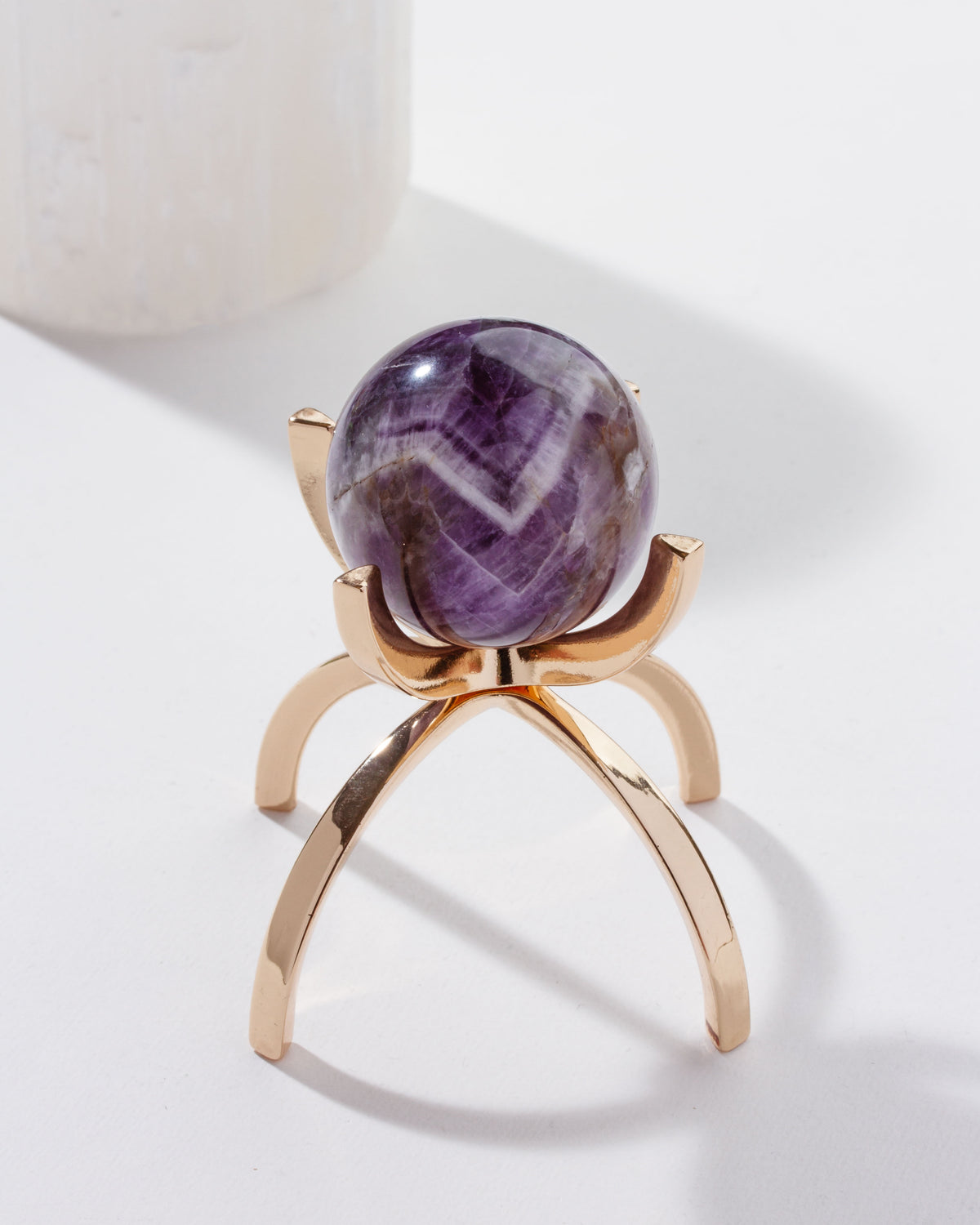 A purple amethyst gemstone sphere on a gold-colored stand, against a white background.