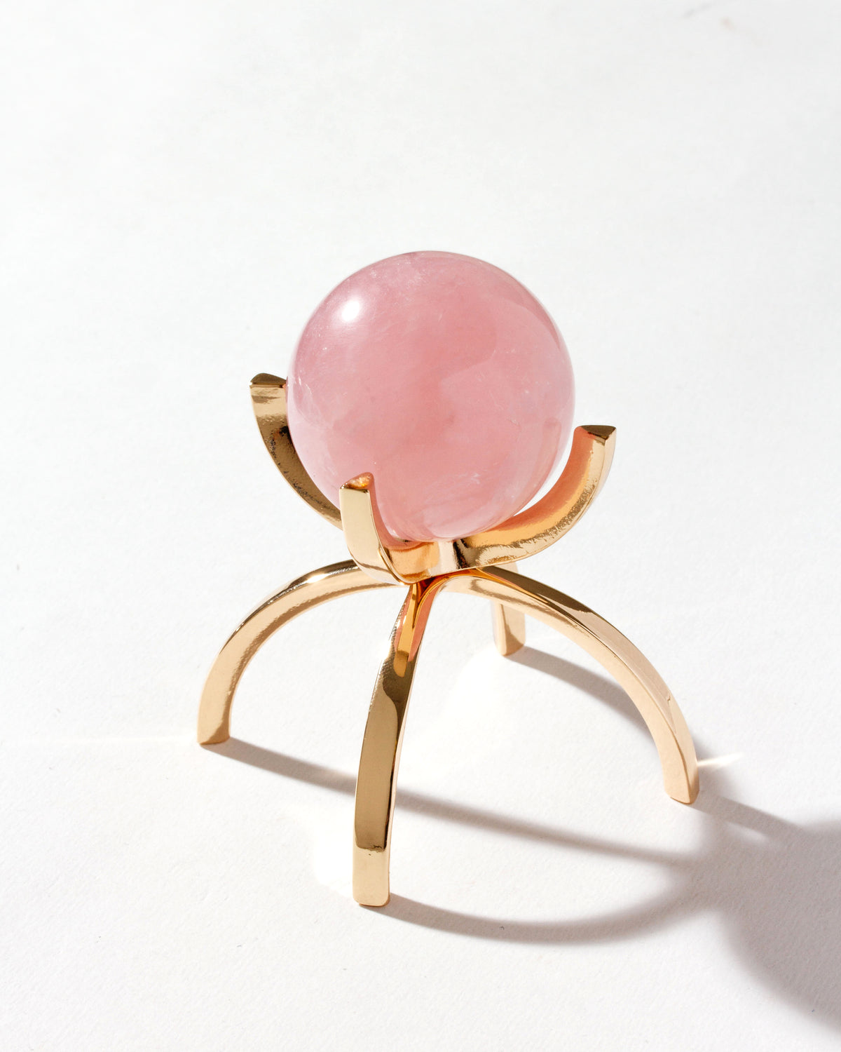 A pink gemstone sphere on a gold-colored stand, on a white background.