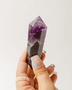 Hand holding a purple Amethyst double point crystal against a white background.