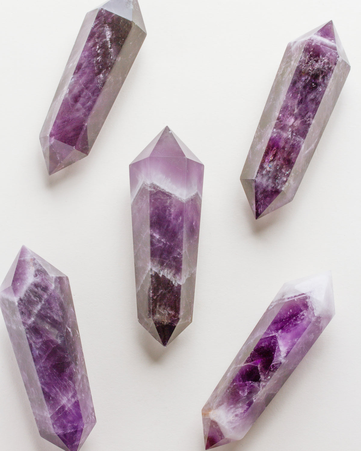 Five Amethyst crystal points laying on a white surface.