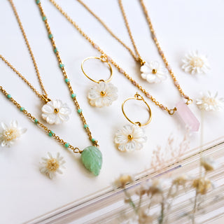 Gold necklaces with green gemstones and white mohter of pearl flowers on a light wooden surface.