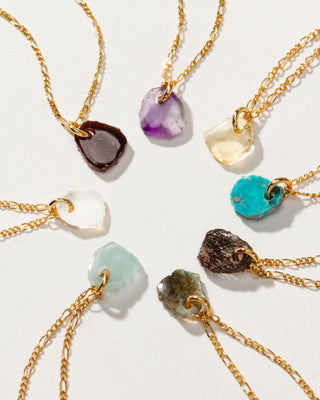 Eight gold necklaces with various colored stone pendants on a white background