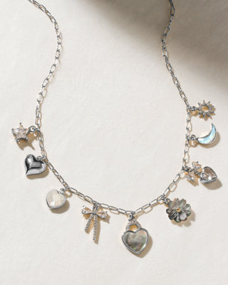 A silver charm necklace with various decorative charms including a heart, a moon, a sun, a flower, and a bow pendant.