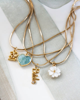 Gold necklaces with Bride, 2025, aquamarine heart, and mother-of-pearl heart charm pendants on a light fabric background