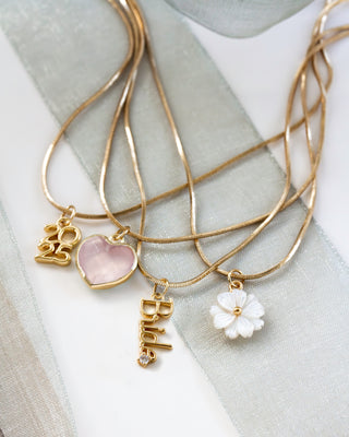 Layered Gold necklaces with Birede, 2025,  rose quartz heart, and mother of pearl charms on a light fabric background