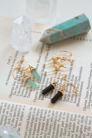 Gold earrings with gemstones on an open book with crystal curios to the side