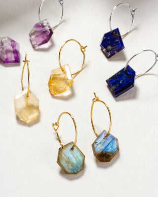 A collection of geometric hoop earrings with various colored gemstones with gold plated wire hoops.