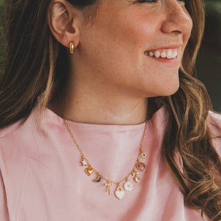 Woman wearing a pink top and gold necklace with charms.