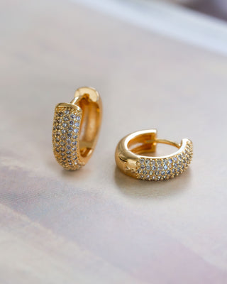 A pair of gold huggie hoop earrings adorned with shimmering pavé CZ stones, displayed against a textured background.
