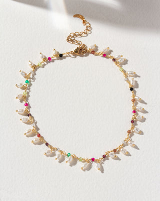 A gold-colored metal anklet with multicolored multistone beads and pearls, displayed against a light background.