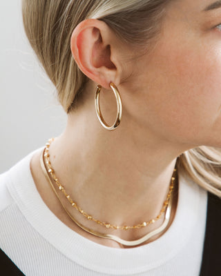 Close-up of a person wearing gold hoop earrings and a gold necklace on a plain background
