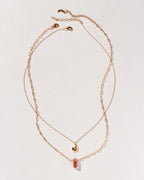 Gold necklaces with strawberry quartz pendant and gold teardrop on plain background