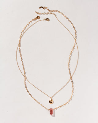 Gold necklaces with strawberry quartz pendant and gold teardrop on plain background