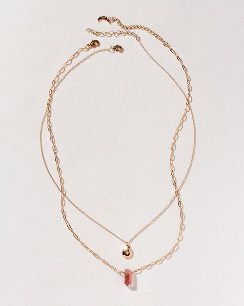 Gold necklaces with strawberry quartz pendant and gold teardrop on plain background