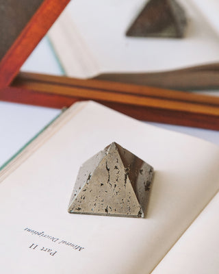 Gold colored Pyrite pyramid curio displayed holding a book page open.