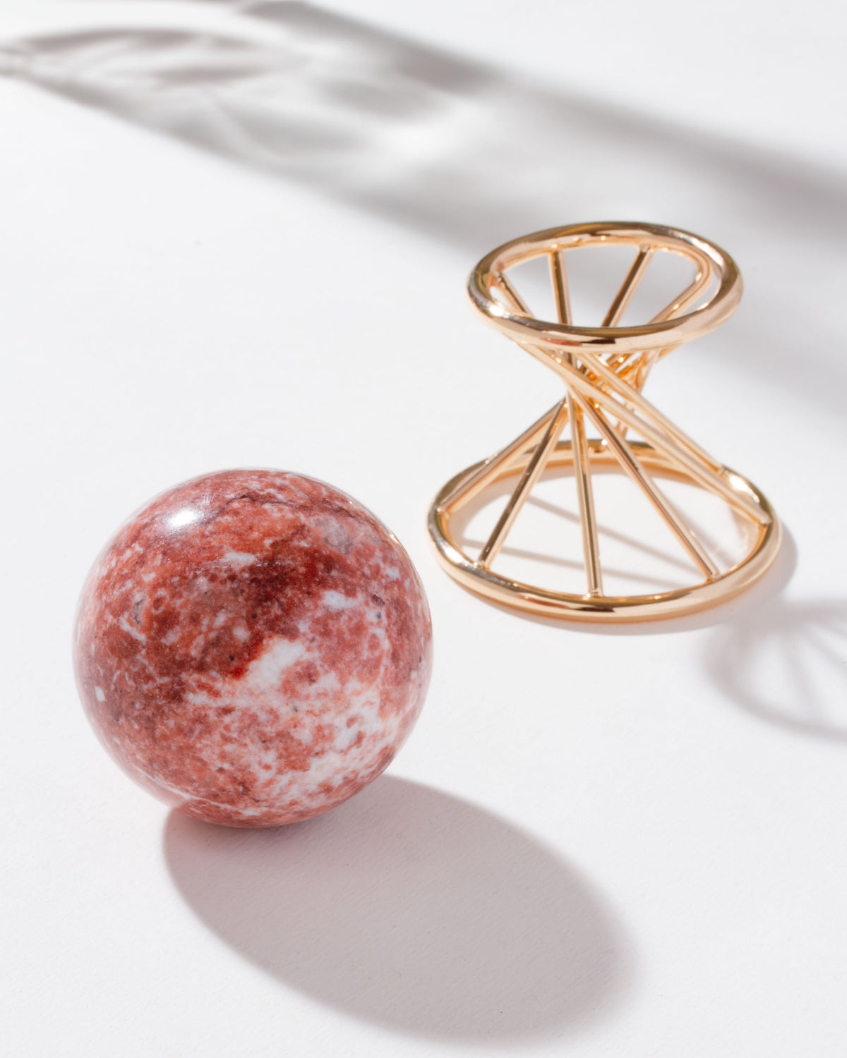 Pink calcite sphere sitting on a white background with a gold stand nearby.