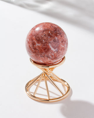 pink calcite sphere sitting on a gold stand against a white background.