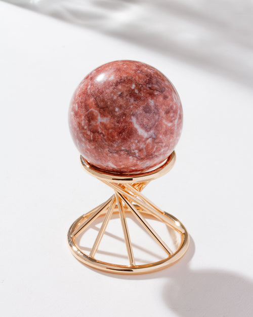 pink calcite sphere sitting on a gold stand against a white background.