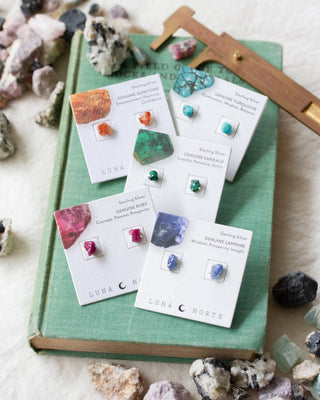 Jewelry cards with gemstone earrings on a green book surrounded by real gemstones.