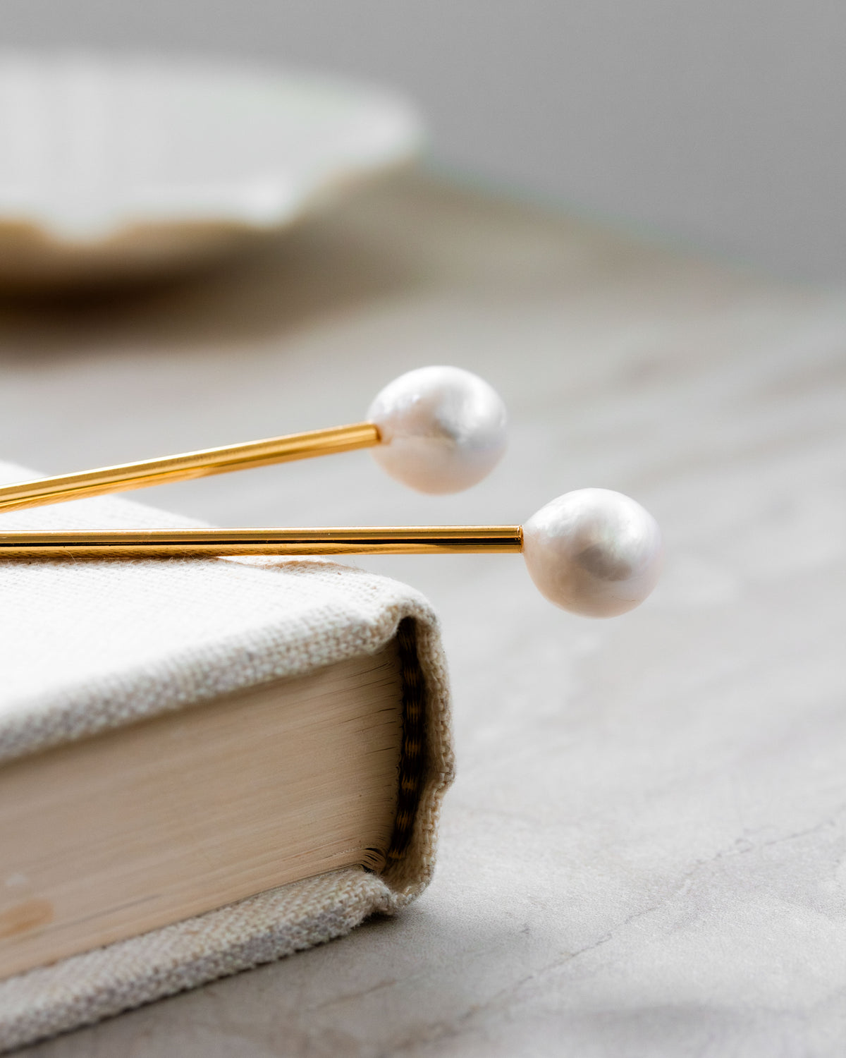 Two Ebb and Flow pearl hair pins with gold-colored metal shanks rest on a book.